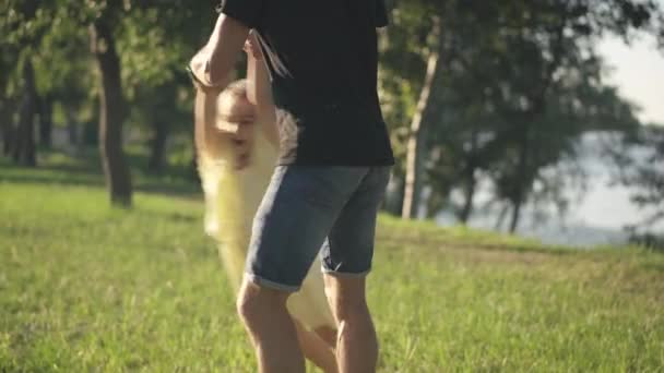 Hombre irreconocible cogido de la mano de una niña girando al sol en el parque de primavera de verano. Alegre padre caucásico divirtiéndose con su hija al aire libre en un día soleado. Ocio familiar y felicidad. — Vídeos de Stock