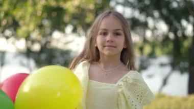 Balonlu oyuncu kız dışarıda gülerken kameraya dönüyor. Yaz tatilinde yaz parkında poz veren sevimli beyaz bir çocuğun portresi..