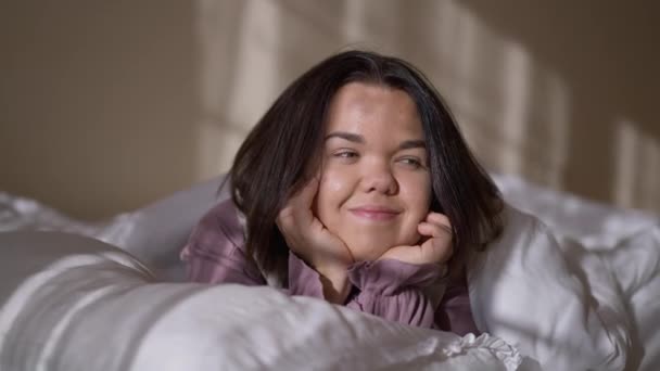 早上穿着睡衣的迷人的年轻女人躺在舒适柔软的床上 面带微笑地望着别处 周末在家里做白种人梦的人的画像 — 图库视频影像