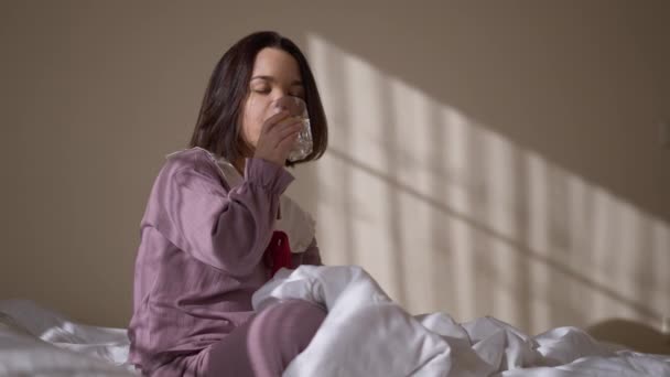 一位自信的白人小妇人坐在床上喝柠檬水 正面微笑的小矮人在室内享受健康维生素饮料的画像 看着窗外 — 图库视频影像