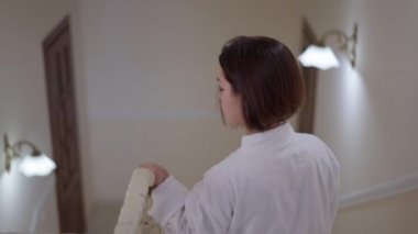 Evinde, aşağıda yürüyen küçük bir kadın. Beyaz bornozlu küçük beyaz bir adam birinci katta yürüyordu.