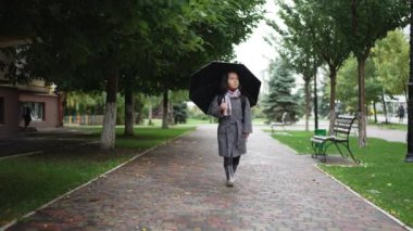 Yağmurlu bir yaz gününde şemsiyesiyle gezen üzgün küçük bir kadın. Şehir caddesinde ağır çekimde yürüyen düşünceli beyaz adamın geniş açılı portresi.