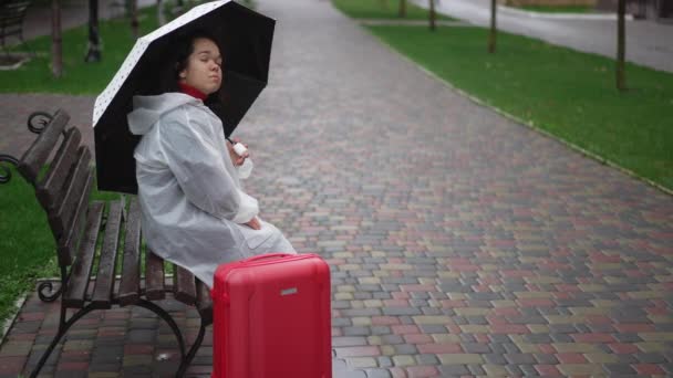 Triste Solitaria Mujercita Con Impermeable Sentada Banco Con Paraguas Maleta — Vídeo de stock