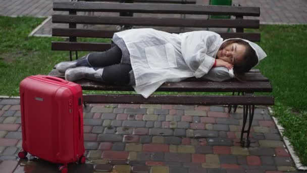 Geniş Açılı Ümitsiz Yağmurluk Giymiş Dışarıda Bankta Uzanmış Seyahat Çantasıyla — Stok video