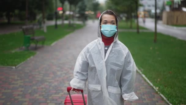 Dolly Yağmurluk Koronavirüs Maskeli Küçük Bir Adamın Şehir Caddesinde Bavulla — Stok video