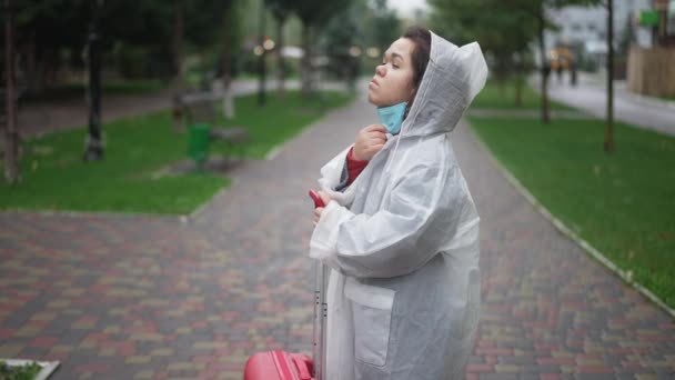 科维德19流感大流行时 身穿雨衣 头戴雨衣 头戴雨衣 头戴旅行袋 呼吸新鲜空气的忧心忡忡的小妇人站在城市街道上 白人小孩喜欢户外旅行的侧景肖像 — 图库视频影像