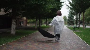 Arkaya bakan genç bir kadın yavaş çekimde yürüyor ve şemsiyesini kaldırıma bırakıyor. Geniş açılı, kaygısız Kafkasyalı küçük insan yağmurlu bulutlu bir günde şehir caddesinde geziniyor.