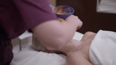 Kapalı gözlü güzel beyaz kadın kozmetik uzmanı olarak kaplıcada uzanıyor ve ağır çekimde yüzüne bal maskesi takıyor. Kendine güvenen müşterinin güzellik merkezinde yaşlanmayı önleme prosedürünü izlemesi