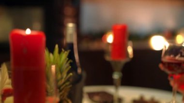 Yakın plan erkek ve kadın elleri kırmızı mumlarla şarap kadehlerini tokuşturuyor. Evde mutlu, tanınmayan bir çiftin yıldönümünü kutluyoruz. Çıkma ve romantizm kavramı