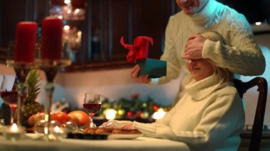 Sağda oturan gülümseyen kadın elleri ve hediyesiyle gözlerini kapatan erkek gibi. Beyaz bir kadın sevgililer gününde kocasına hediye ettiği için teşekkür ediyor. Kutlama ve romantizm