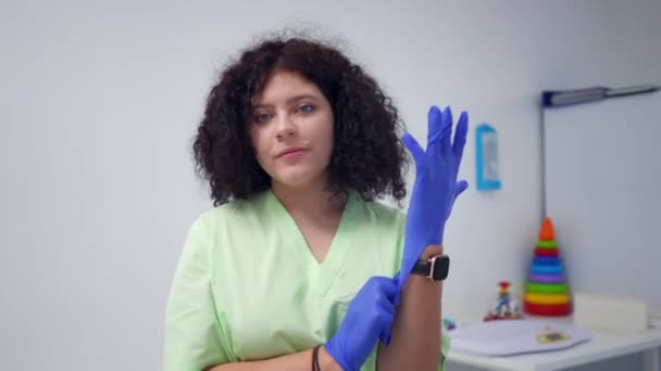 Portrait Positive Pediatrician Looking Camera Putting Gloves Smiling Young Caucasian — Stockvideo