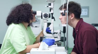 Hastanedeki retina kamerasıyla göz arkasını kontrol eden yoğun bir doktor. Kafkasyalı hasta, göz hastalıkları kliniğinde cihaz kullanarak profesyonel uzman olarak ekipman başında oturuyor.