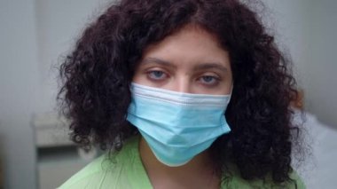 Close-up exhausted face of tired doctor in coronavirus face mask looking at camera. Overburdened Caucasian young woman posing in hospital indoors on Covid-19 pandemic outbreak
