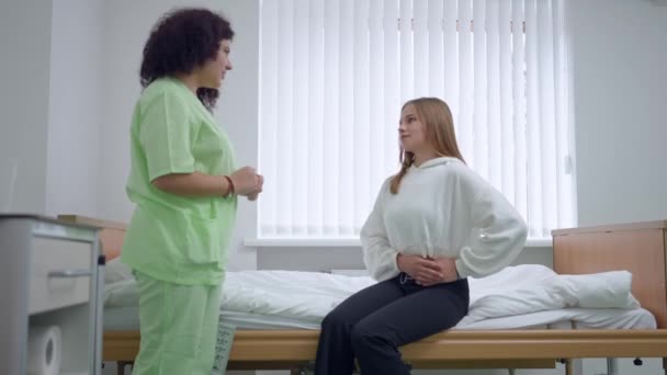Молодая Женщина Жалуется Боль Сидя Палате Разговаривая Медсестрой Стоящей Больнице — стоковое видео