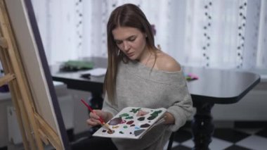 Sıska bir kadının orta boy portresi. Paletin renklerini karıştırıyor. Titreyen baş iç geçiriyor. Tatmin olmamış, beyaz tenli sanatçı ilham perisini kaybediyor. Tabloda oturup düşünüyor.