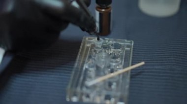 Elleri eldivenli, siyah kalıcı dövme mürekkebi damlatan yakın çekim güzellik aletleri. Tanımlanamayan profesyonel makyaj ustası güzellik salonunda işlem için aletler hazırlıyor.