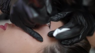 Kapalı bir güzellik salonunda mikropatenli kalemle yakın plan dövmeli kaş. Yüz derisine mürekkep süren güzellik uzmanı eli olan beyaz bir kadının yüzü. Kalıcı makyaj konsepti
