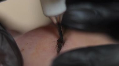Extreme close-up filling eyebrow skin with pigment using microblading pen in beauty salon. Unrecognizable tattoo master hands in gloves tattooing Caucasian young woman. Dermapigmentation concept
