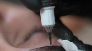Yakın plan mikropatenli, iğneli, kaş dövmeli bir kalem. Tanımlanamayan beyaz kadın güzellik salonunda eldivenli profesyonel güzellik uzmanı olarak yatıyor ve kalıcı makyaj yapıyor.