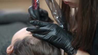 Unrecognizable concentrated beautician tattooing eyebrows of Caucasian woman doing permanent makeup in beauty salon. Blurred client talking to professional expert lying indoors
