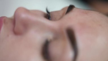 Güzellik salonunda sürekli kaş dövmesi yapan zayıf bir kadının yakın çekimi. Tanınmayan güzellik uzmanları eldiven giymiş ellerinde mikroplu patinaj şekillendirme aleti var. Deriye mürekkep enjekte ediyorlar.