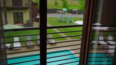 High angle view sunbeds at pool outdoors at tourist resort on summer day. View from hotel room at comfortable neat furniture behind handrails. Slow motion
