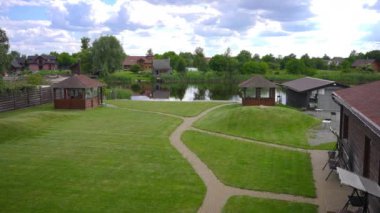 Wide shot beautiful landscape on eco-resort with wooden biuldings green meadow and lake. Scenics in tourist resort outdoors. Tranquility and eco-tourism concept
