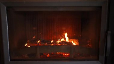 Front view glass door of fireplace with red flame burning inside. Close-up cozy comfortable luxurious domestic decoration indoors with no people. Tranquility concept