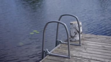 Close-up steel handrails on wooden pier with blue water flowing. Calm river with deck outdoors on summer day