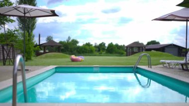 Blue clear water in swimming pool with reflection of cloudy summer sky. Wide shot calm eco-resort outdoors with no people. Slow motion