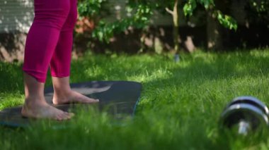 Side view legs of plus-size sportswoman jumping on exercise mat in summer garden on the left. Unrecognizable Caucasian overweight barefoot woman working out training outdoors on sunny day