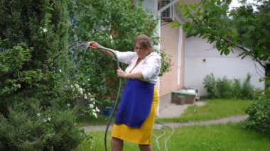 Joyful carefree plus-size woman having fun spinning water hose jumping in slow motion outdoors. Portrait of happy relaxed Caucasian gardener enjoying hobby on summer day