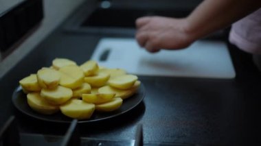 Close-up plate with halved potato and male Caucasian hand taking piece cutting it with knife in slow motion. Unrecognizable man cooking tasty lunch indoors in kitchen. Culinary and cuisine concept