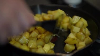 Male hand stirring potato frying on cooking pan on kicthen stove indoors. Unrecognizable Caucasian young man cooking delicious tasty dinner at home