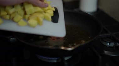 Close-up male hand putting potato squares on frying pan with boiling sunflower oil. Unrecognizable Caucasian man cooking tasty delicious dinner indoors in kitchen. Culinary and food concept