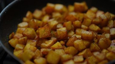 Close-up green dill falling on cooked fried potato in cooking pan with boiling oil. Unrecognizable person preparing delicious breakfast in kicthen at home indoors. Food and taste concept