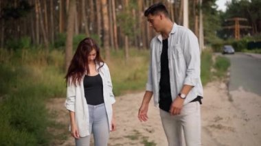 Nervous young man arguing with woman hitchhiking with Future banner. Portrait of dissatisfied Caucasian boyfriend tired of travelling with carefree girlfriend talking standing at forest on suburb road