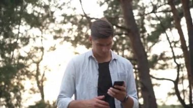 Worried anxious man searching mobile network raising smartphone standing in forest. Portrait of Caucasian handsome tourist lost outdoors. GPS and adventures concept