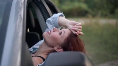 Side view face of happy beautiful woman sitting in car leaning on door looking up. Relaxed attractive Caucasian traveler enjoying trabquility and leisure in forest outdoors