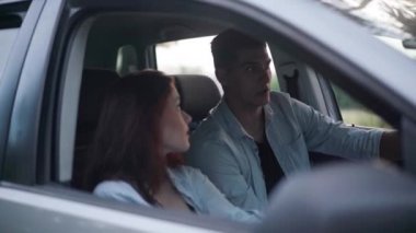 Young positive couple sitting in car discussing trip route. Happy loving Caucasian boyfriend and girlfriend chatting smiling choosing direction. Travelling and togetherness concept