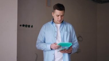 Thoughtful man with digital tablet standing in new apartment looking around thinking. Portrait of focused concentrated Caucasian flat owner planning renovation and repair indoors