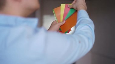 Close-up color palette in hands of unrecognizable man choosing walls color. Young Caucasian flat owner planning renovation standing in apartment indoors thinking