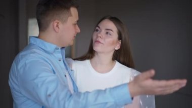 Young charming woman hugging loving man explaining renovation plan talking standing in new flat. Portrait of happy Caucasian millennial couple moving in apartment planning repair