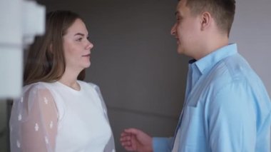 Side view positive happy couple talking gesturing high-five standing in new flat. Loving young Caucasian man and woman discussing renovation planning moving in apartment