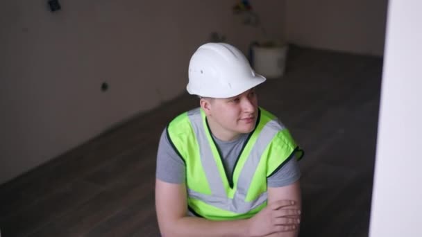 Young Man Hard Hat Green Vest Sitting Floor New Apartment — Stockvideo