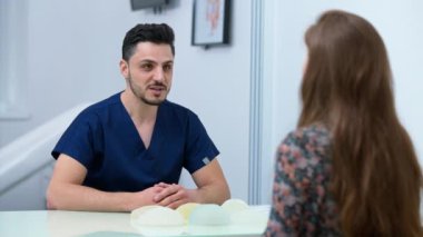 Portrait of handsome Middle Eastern doctor talking with patient smiling sitting in hospital indoors. Professional positive man consulting woman in medical clinic. Health care and insurance concept