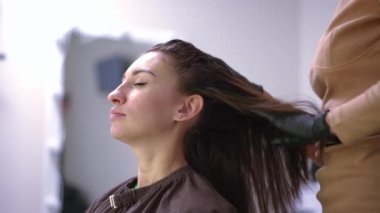 Side view woman enjoying head massage in hair parlor indoors looking away. Satisfied Caucasian female client and unrecognizable expert cosmetician in gloves in beauty salon