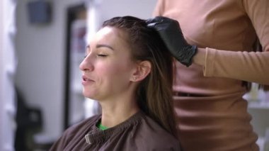 Side view positive beautiful woman talking with unrecognizable hairdresser massaging head applying moisturizing conditioner. Happy satisfied Caucasian client chatting with professional hairstylist