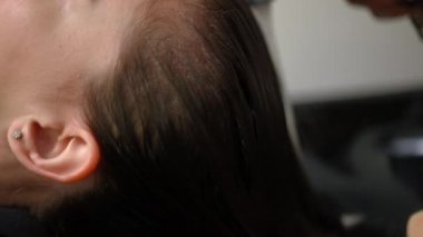 Zoom out from long hair of brunette woman with water flowing in sink. Side view of slim beautiful Caucasian client in beauty parlor with unrecognizable hairdresser washing head