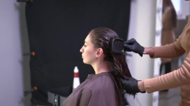 Side view gorgeous client in beauty parlor with unrecognizable hairstylist combing long clean wet hair with brush. Caucasian confident woman doing hairdo in hair salon. Femininity and lifestyle